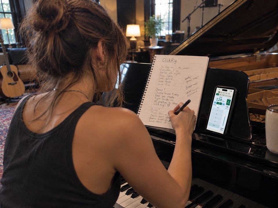 Songwriter at a piano with a notebook and ClickRig on an iPhone.